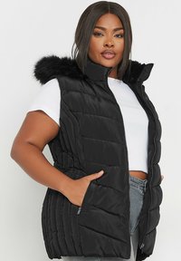 Mustat puffertitakki, jossa on korkea kaulus, vetoketjukiinnitys ja tekoturkisreunus hupussa. Ominaisuuksiin kuuluvat vaakasuorat tikkaukset ja kaksi sivutaskua.