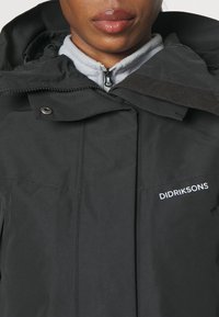 Giacca impermeabile nera con zip davanti, chiusure a scatto e colletto alto. Logo "DIDRIKSONS" sul petto.