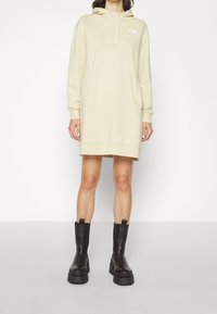 Ljust gul hoodieklänning med framsida fickor och justerbar dragsko på huvan, kombinerad med svarta klumpiga ankelskor.