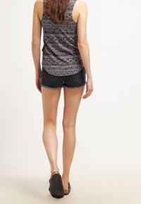 Top sin mangas de patrón en gris con diseños geométricos, combinado con pantalones cortos de mezclilla oscuros con bordes deshilachados y sandalias planas.