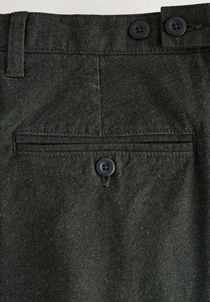 Szczegóły ciemnoszarych wełnianych spodni z dwoma czarnymi guzikami w pasie oraz jednym guzikiem zapięcia poziomej tylnej kieszeni.