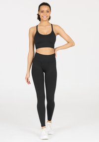 Schwarzes sportliches Crop-Top und hoch taillierte Leggings, beide aus dehnbarem Material. Getragen mit weißen Sneakers, die eine glatte Textur und ein minimales Design aufweisen.
