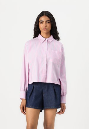 Cropped button-up shirt in light pink with blue stripes, featuring long sleeves and a chest pocket; paired with dark denim shorts.