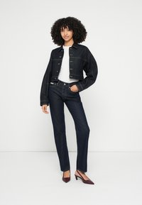 Ciemna dżinsowa kurtka o kroju crop z zapięciem na guziki, zestawiona z ciemnymi jeansami o prostych nogawkach. Pod spodem biała koszula oraz bordowe czółenka na szpilce z ostro zakończonym noskiem.