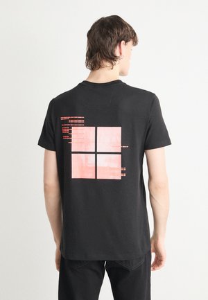 T-shirt en coton noir avec un design graphique rouge au dos, composé de quatre carrés et de lignes horizontales. Manches courtes et encolure ronde.