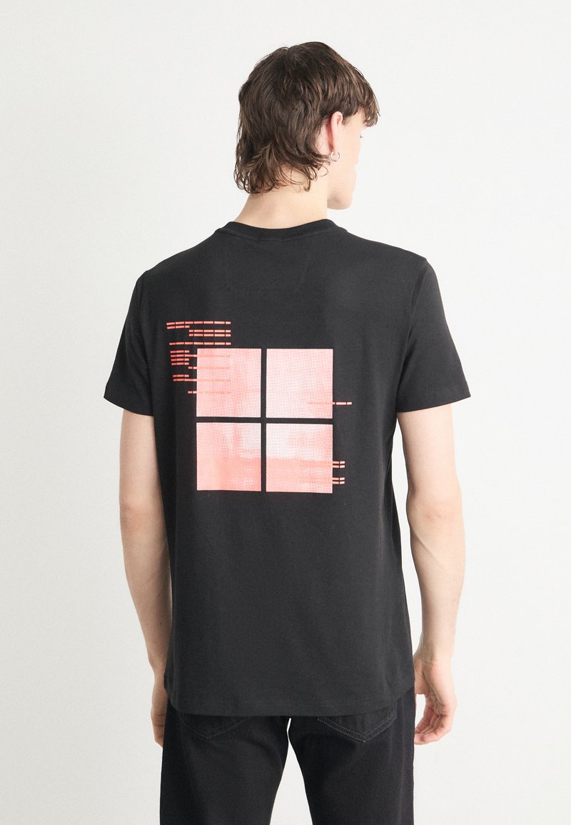 T-shirt en coton noir avec un design graphique rouge au dos, composé de quatre carrés et de lignes horizontales. Manches courtes et encolure ronde.