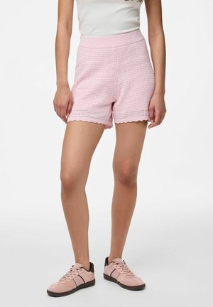 Lyserøde strikkede shorts med en bølget kant, der har en ribbet talje. Sammen med lyserøde sneakers, der viser bløde teksturer.