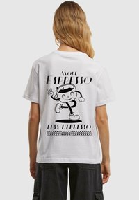 Valkoinen puuvillainen t-paita, jossa on sarjakuvamainen kahvikuppigrafiikka ja teksti "More Espresso Less Depresso" mustana. Yksinkertainen, rento muotoilu.