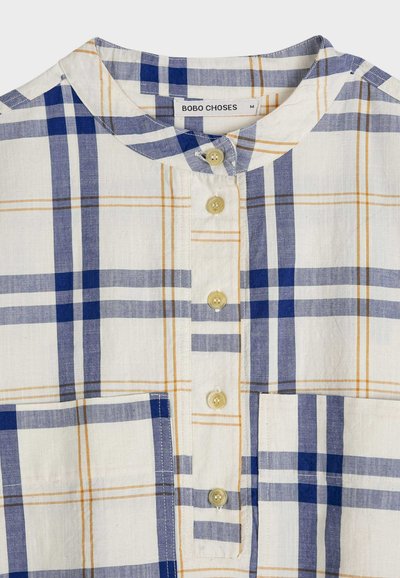 Chemise à col avec motif à carreaux bleu, marine et beige, boutons beiges sur le devant et deux poches frontales.