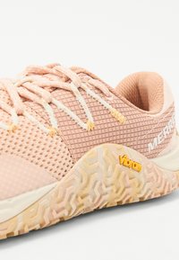 Zapatilla de malla rosa claro con detalles estampados, suela de goma texturizada y logo amarillo de Vibram en el costado. Los cordones son de un color beige claro.