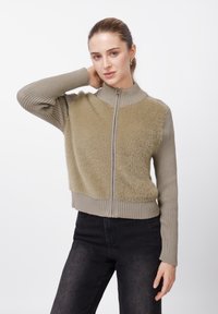 Φούτερ με φερμουάρ σε ανοιχτό πράσινο ελιάς, με υφή αφράτου υφάσματος στο σώμα και ριμπ μανίκια, με ψηλό γιακά και εφαρμοστή μέση.