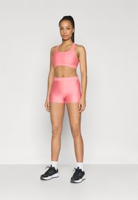 Rózsaszín sportos crop top és rövidnadrág sima, rugalmas anyagból, logóval díszítve és testhezálló kialakítással.