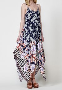 Robe maxi florale marine avec un profond décolleté en V, bretelles spaghetti réglables et un ourlet fluide orné d'une bordure à motifs. Sandales à plateforme marron.