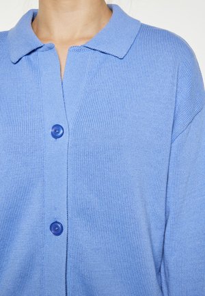Cardigan tricotat albastru cu textură ribbed, având guler și două butoane mari albastre în față. Material moale și ușor.