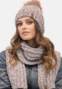 Strickmütze mit einem rosa Pompon und einem strukturierten Schal, beide in Creme- und Rosatönen, mit einem braunen Logoetikett.