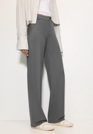 Person wearing gray wide-leg trousers, white sneakers, a white cropped top, and a light-colored striped long-sleeve shirt.