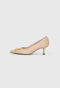 Décolleté beige con tacco alto realizzato in materiale sintetico liscio, con punta appuntita e una fibbia decorativa gialla sul davanti.