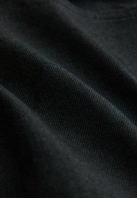 Black knit fabric, featuring a smooth texture with slight elasticity; visible folds and ridges highlight its lightweight design.