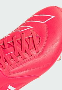 Scarpa da calcio rosa brillante realizzata in cuoio testurizzato, con cuciture e lacci bianchi, punta liscia e tacchetti conici sulla suola.