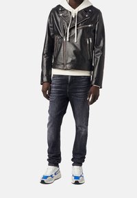 Svart lädermotorcykeljacka med silverdragkedjor, i kombination med en vit huvtröja, mörka slim fit-jeans och sneakers med blå accenter.