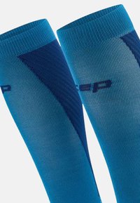 Calze a compressione in una gradazione di blu chiaro a blu scuro, con una texture a coste e un logo in blu scuro a contrasto.