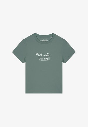 T-shirt en coton vert avec des manches courtes et un col rond. Présente le texte blanc "Ich zähl bis drei !" sur le devant.