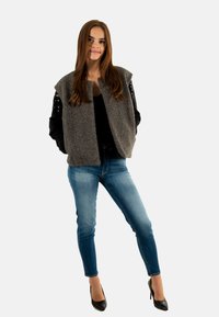 Gilet en mélange de laine gris avec des manches ornées de sequins noirs, associé à un jean skinny bleu clair et des escarpins noirs à bout pointu.