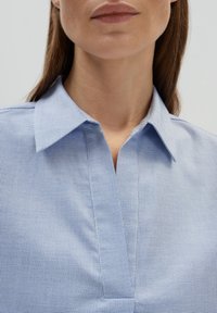 Camicia azzurra chiara con colletto, caratterizzata da un motivo a quadri piccoli e texture. Il tessuto è liscio con una finitura leggermente lucida e una vestibilità comoda.