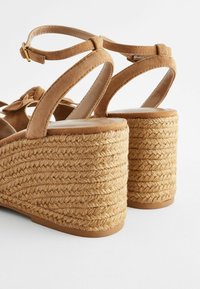 Braune Wildleder-Wedge-Sandalen mit einem geflochtenen Jute-Absatz, die über Kreuz angeschnallte Riemen und eine Schleifenverzierung am vorderen Riemen verfügen.