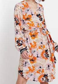 Blommig omlottklänning med rosa, orange och svarta blommönster. L�ånga ärmar med randiga manschetter; lätt, svävande tyg.
