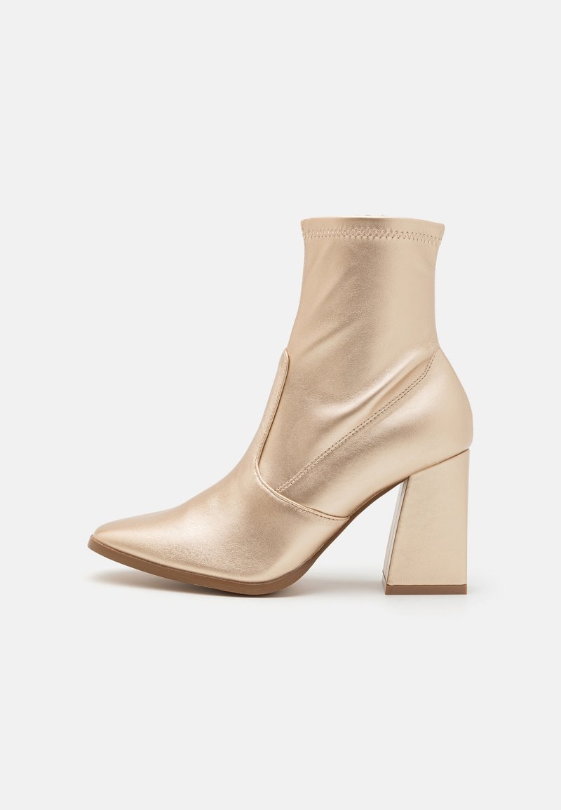 Bottes métalliques dorées à la cheville avec un bout pointu, un talon bloc haut, et une coupe ajustée avec des détails de couture visibles. Texture lisse sur toute la surface.