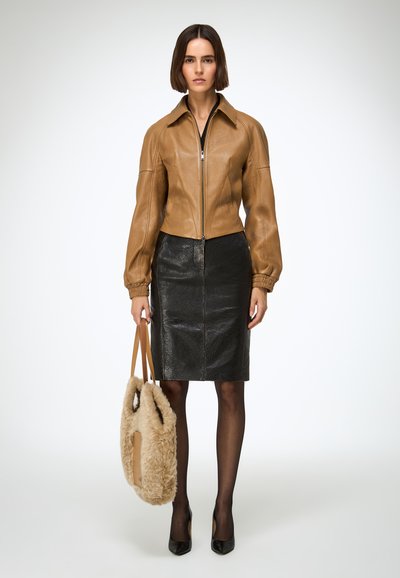 Barna bőr rövidített dzseki gallérral, fekete műbőr ceruzaszoknyával párosítva. Texturált kialakítás jellemzi és egy bolyhos bézs táska kíséri.