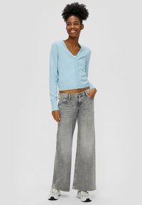 Jasnoniebieski krótki kardigan z dekoltem w serek i guzikiem z przodu, w połączeniu z szerokimi szarymi dżinsami. Posiada prążkowane mankiety i pas.