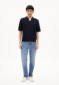 Marineblauwe gebreide polo met korte mouwen en een V-hals, gecombineerd met lichtblauwe rechte jeans en witte sneakers. Eenvoudige ribbelstructuur.