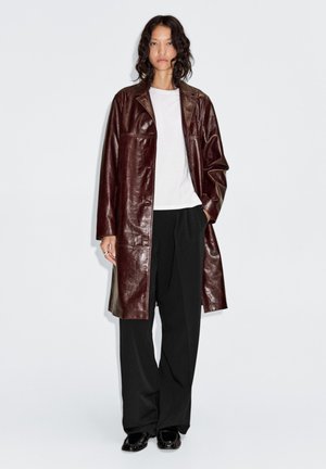 Vinröd läderrock med avslappnad passform, med krage, långa ärmar och en slät yta. Bärs över en vit t-shirt och svarta byxor.