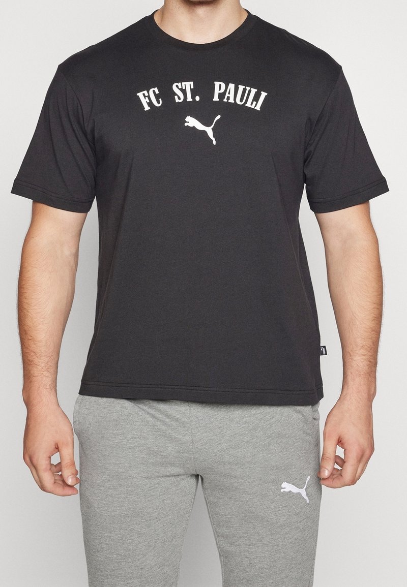 Černé bavlněné tričko s nápisem "FC ST. PAULI" a bílým logem Puma. Jednoduchý design s kulatým výstřihem a krátkými rukávy. Spárováno se šedými tepláky.