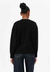 Zwarte gebreide trui met een ronde hals, dropped shoulders en geribbelde mouwuiteinden. Draagt met donkerdenim jeans, gezien vanuit de achterkant.