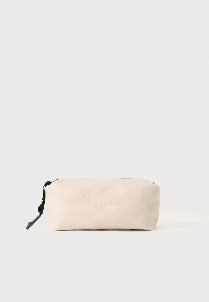 Funda de cuero beige con una textura suave, forma rectangular y un tirador de cremallera negro. Presenta el logotipo en relieve "STUTTERHEIM".