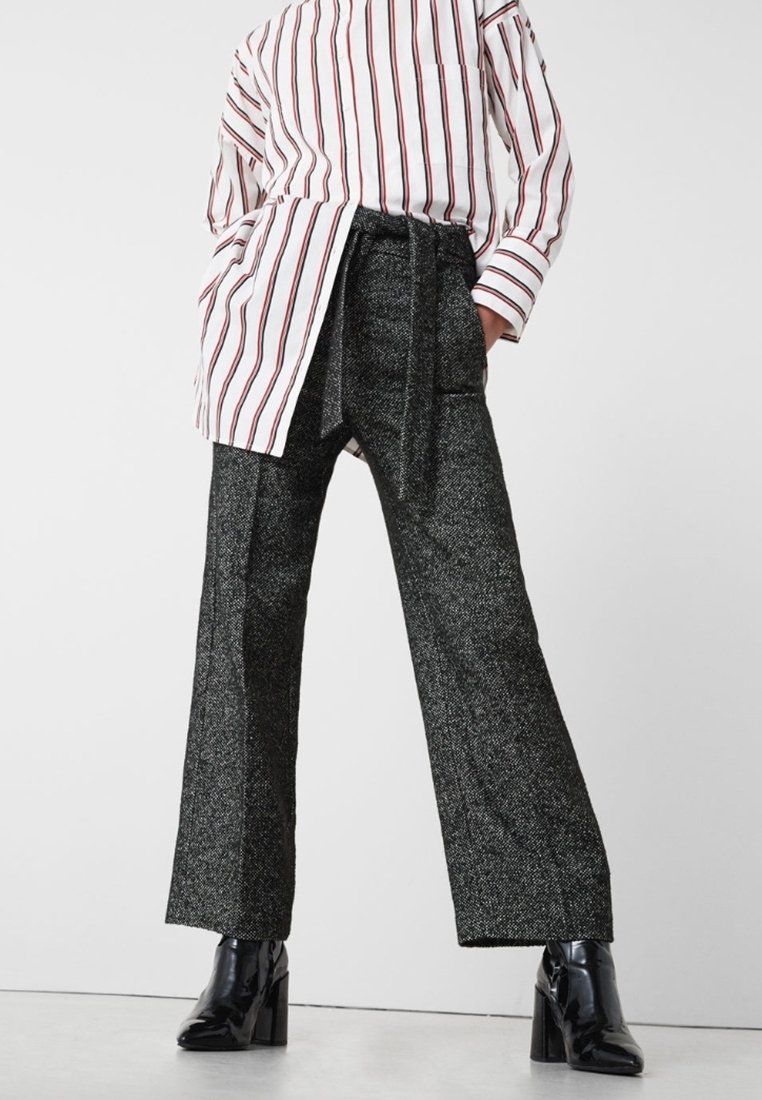 Personne portant un pantalon noir à jambes larges texturé avec une ceinture, une chemise blanche à manches longues avec des rayures rouges, et des bottes noires à talons.