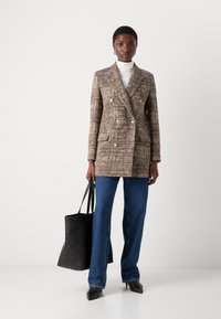 Brauner Fischgrät-Doppelreiher-Blazer mit goldenen Knöpfen, zwei Vordertaschen, kombiniert mit blauen weit geschnittenen Jeans und einer schwarzen Tragetasche.
