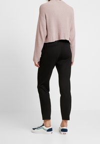 Roze gebreide cropped trui, zwarte slim-fit broek en sneakers met blauwe en crème accenten. Zichtbare textuur en geribbelde details op de trui.