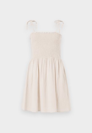 Bézs színű, ujjatlan ruha fodros mellel, állítható kötőkkel és bővülő szoknyával. Könnyű, texturált anyagból készült.