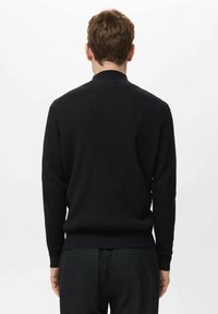 Jersey negro de punto con textura acanalada, con un cuello redondo y mangas largas. La vista trasera muestra un diseño minimalista y un dobladillo ajustado.