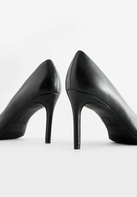 Décolleté nere in pelle con tacco alto, punta affilata, texture liscia e sottile tacco a stiletto. Presentano un marchio discreto sulla suola.