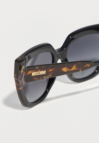 Γυαλιά ηλίου με μαύρο τετράγωνο πλαίσιο, σκουρόχρωμους φακούς και μπράτσα από μοτίβο χελώνας, με το χρυσό λογότυπο Moschino.