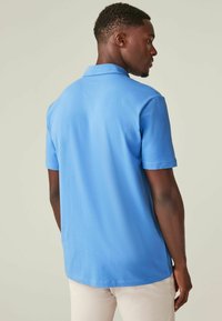 Himmelblaues Poloshirt mit kurzen Ärmeln, klassischem Kragen, glatter Textur und entspannter Passform, von hinten gesehen.