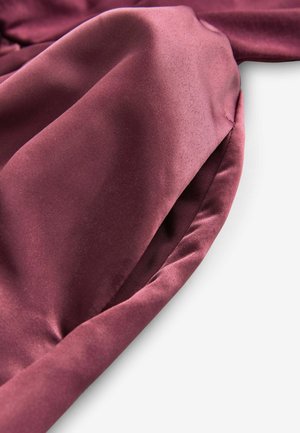 Bordeaux stof die een gladde, satijnen textuur toont met een lichte glans, elegant vallend en met geplooide details langs de randen.