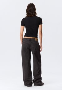 Schwarze Jeans mit weitem Bein und hoher Taille, ausgestattet mit zwei Gesäßtaschen und einem braunen Lederetikett am Bund. Strukturierter Stoff.