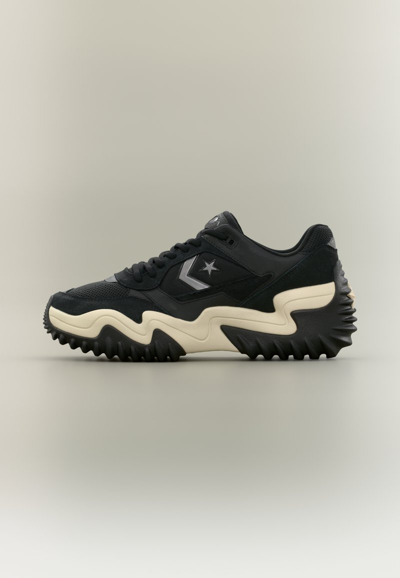 Must tennisejalanõu beeži lainelise tallaga, küljes tähe ja siksaklogo, tekstureeritud tallaga ning võrkkangast ja seemisnahast pealiskihiga ühtlasel taustal.