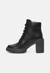 Botas de cuero negro hasta el tobillo con un tacón ancho, cordones en la parte delantera y suela texturada. Presentan un collar acolchado y un acabado suave.